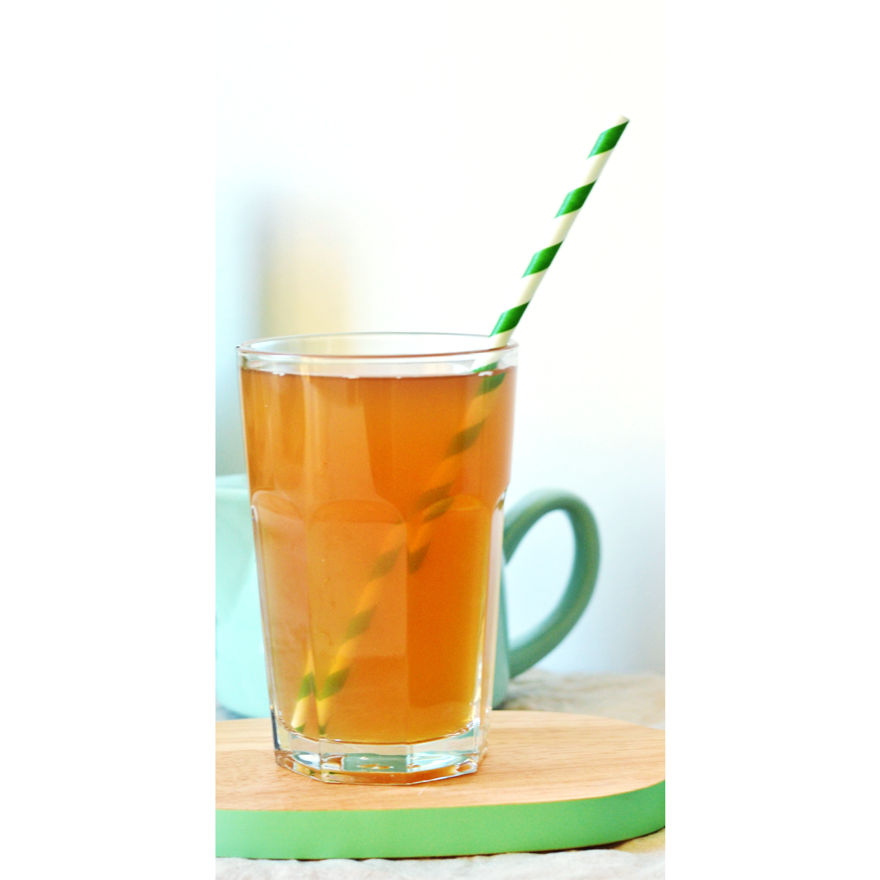 Un verre de thé avec une paille verte et blanche, sur une planche ronde en bois