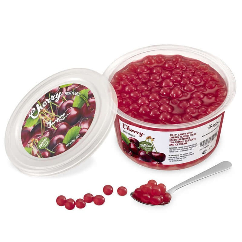 Une boite sur fond blanc remplie de perles rouges et à gauche le couvercle avec plusieurs cerises. Devant des perles rouges dans une cuillère
