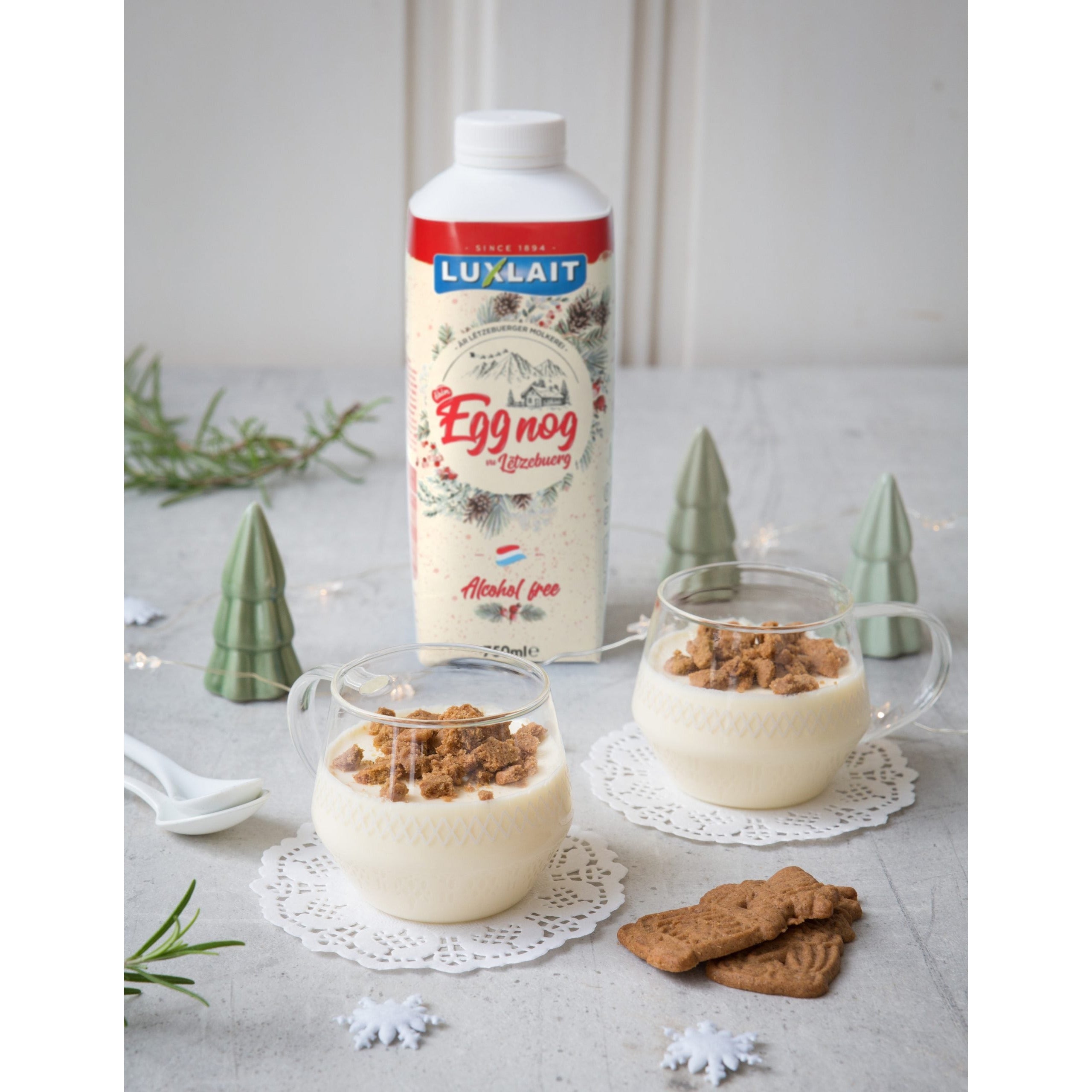 Une bouteille en carton de Luxlait sur une table avec des décorations de Noel et devant 2 tasse transparent avec une yaourt et des copeaux de Spéculoos