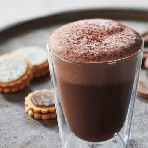 Un verre transparent de chocolat chaud et 3 biscuits en arrière-plan