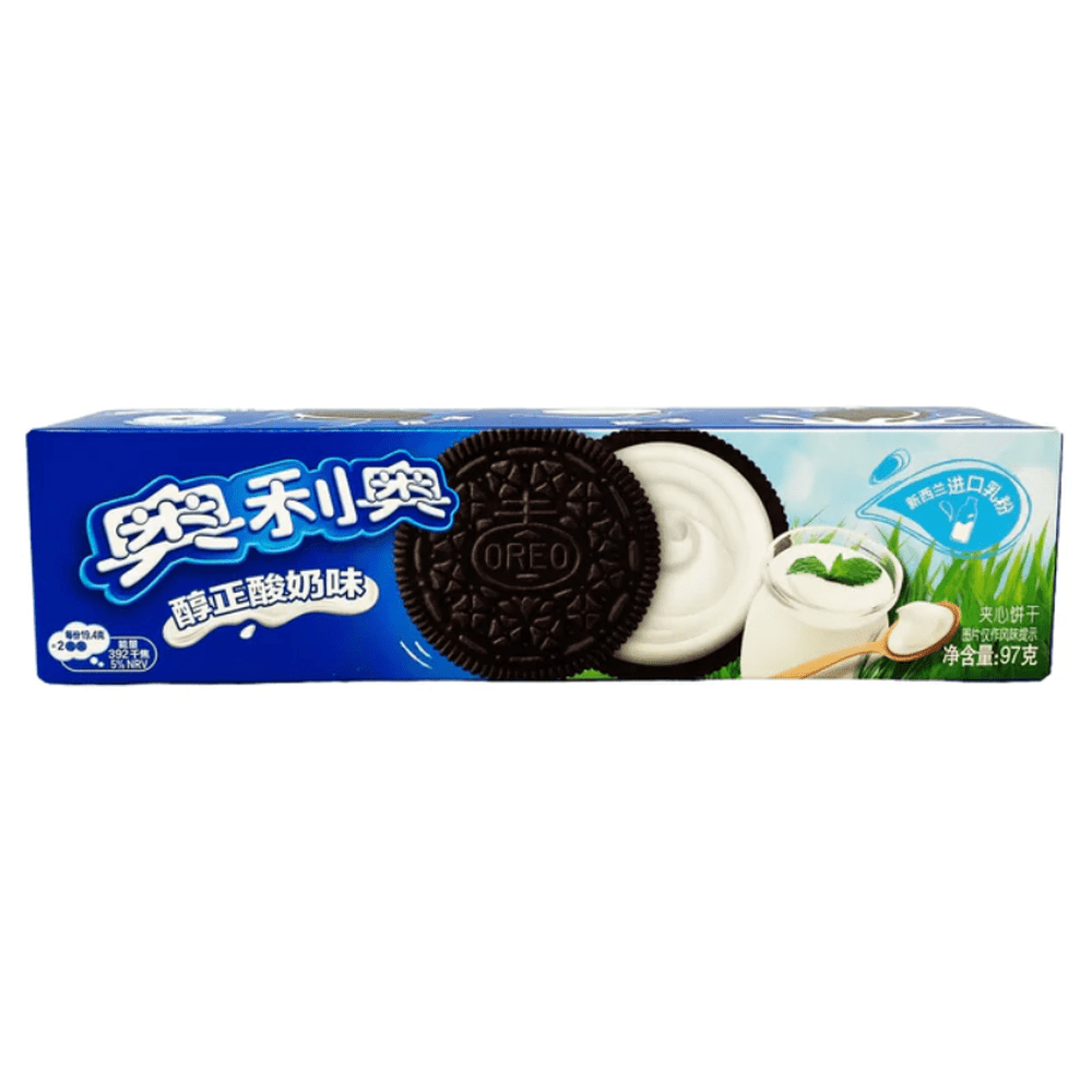 Un emballage long bleu sur fond blanc avec un biscuit noir ouvert et il y a une crème blanche, à droite un pot en verre de yaourt blanc et à coté de l’herbe verte