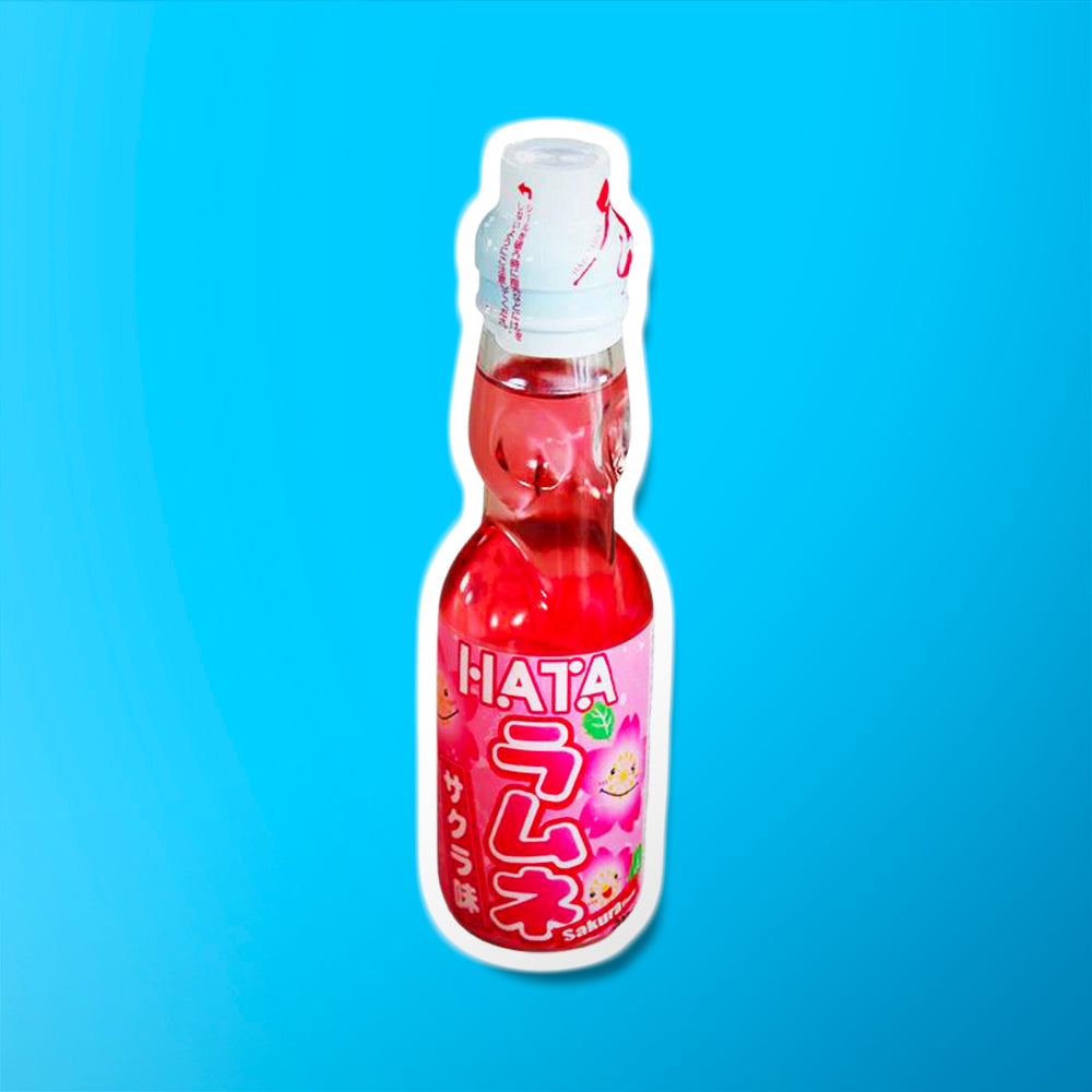 Une bouteille transparente sur fond bleu avec une boisson légèrement rosée, il y a une étiquette rose sur la moitié basse de la bouteille. Il y a des fleurs de cerisiers qui sourient