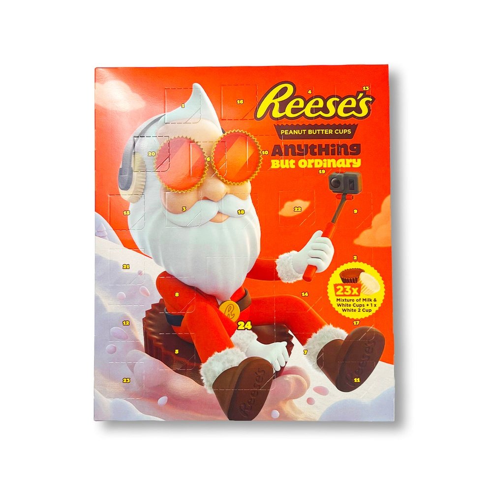 Un emballage orange sur fond blanc avec un père Noël stylé qui se filme entrain de descendre une montage enneigée assis sur un chocolat Reese’s géant 