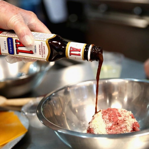 Une main verse la sauce en bouteille noire sur un viande qui est dans un saladier en acier inoxydable