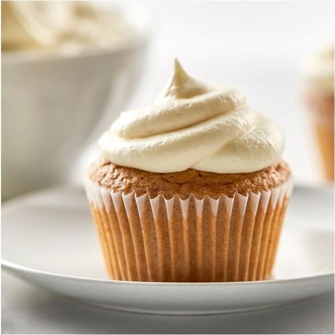 Un cupcake nature dans son papier transparent et un glaçage couleur crème, dans une assiette blanche