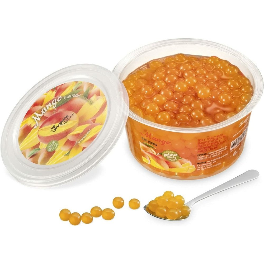 Une boite sur fond blanc remplie de perles oranges et à gauche le couvercle avec plusieurs mangues. Devant des perles oranges dans une cuillère