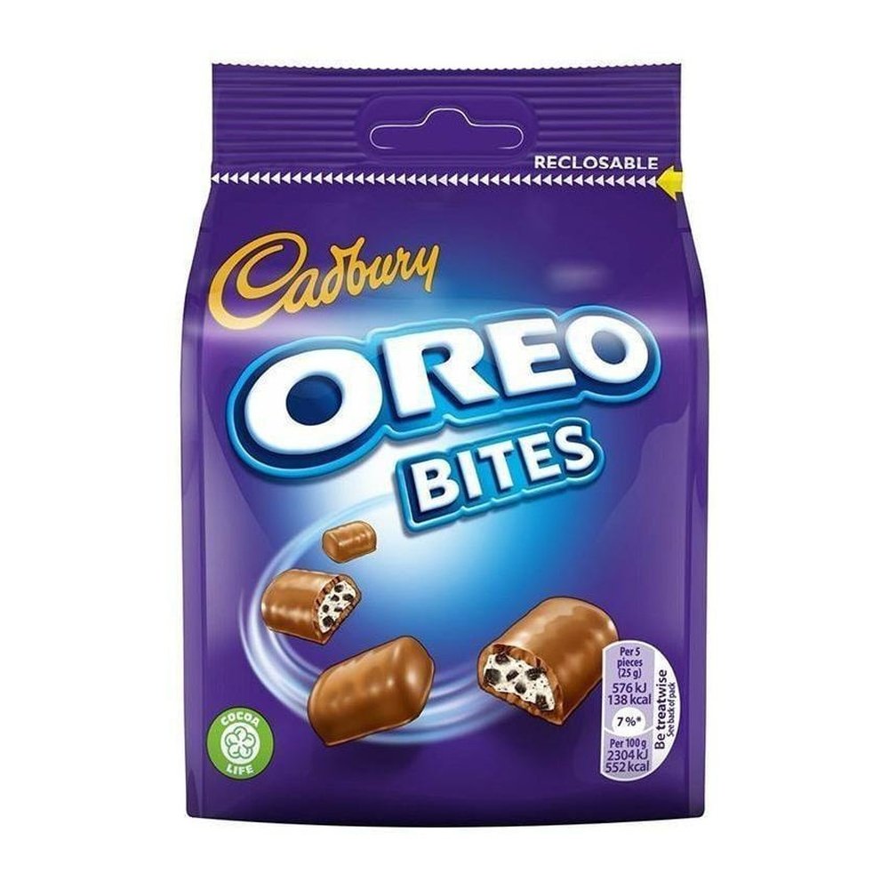 Un emballage mauve sur fond blanc avec des morceaux de chocolat et on y voit leur intérieur qui sont blanc et avec des morceaux de biscuits noirs