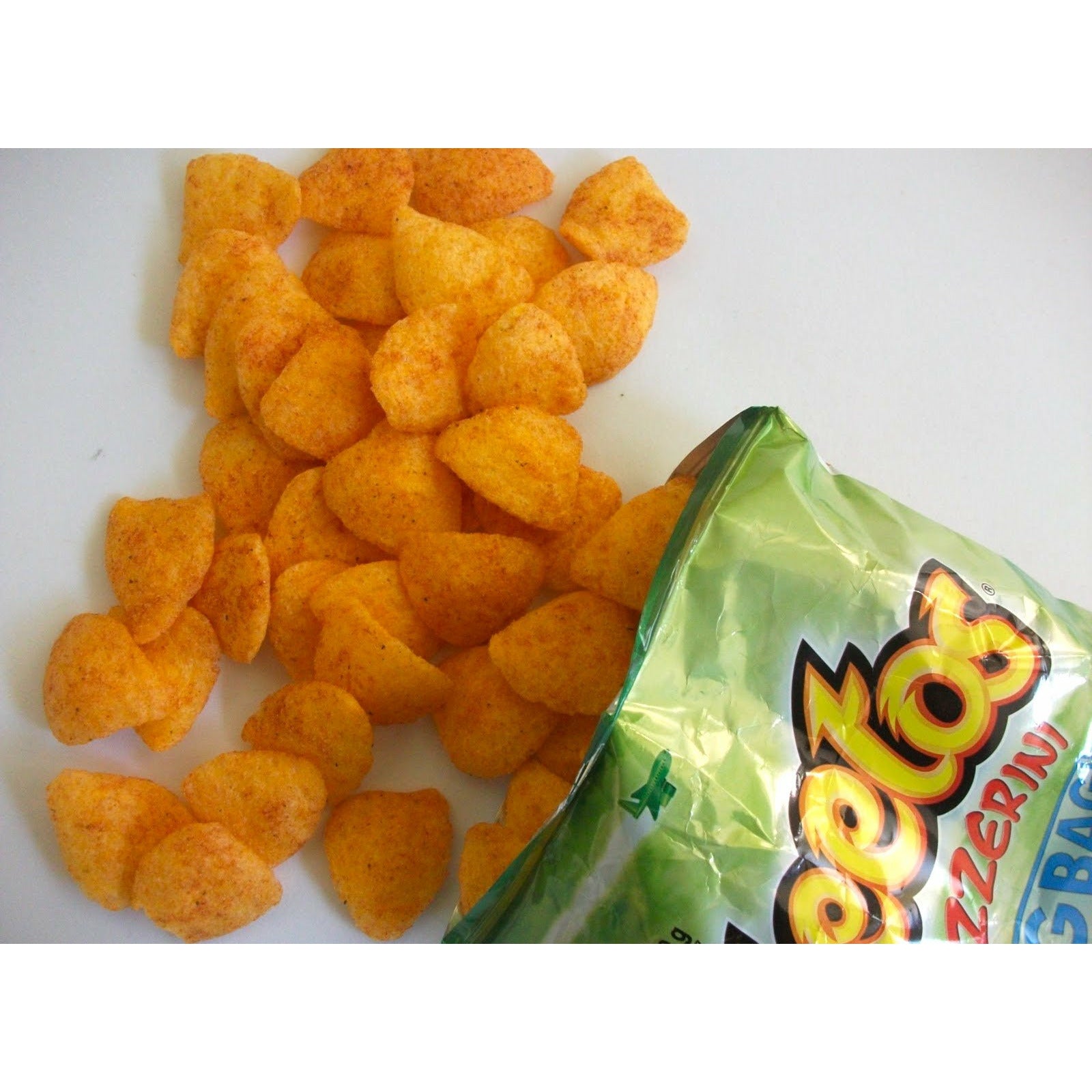 Un paquet vert ouverte et plein de chips oranges de forme triangulaire vus dans haut et sur une table blanche 