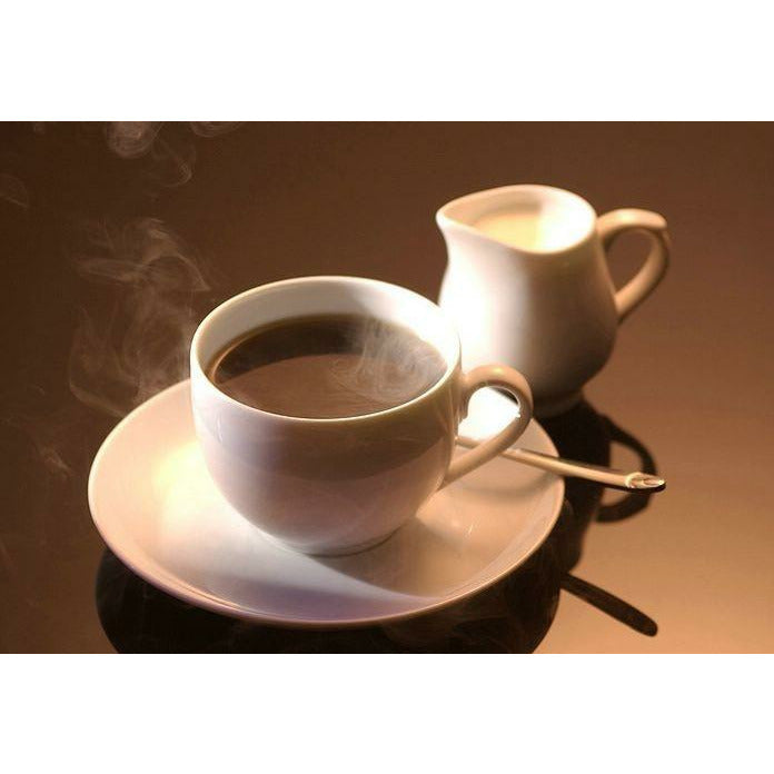 Une tasse blanche de café sur une assiette blanche et à coté un récipient avec une crème, le tout sur une table noire