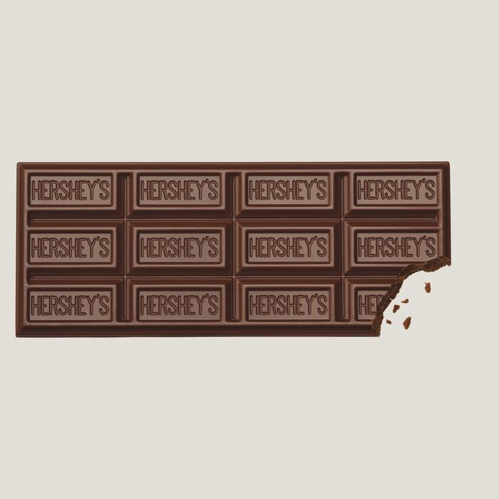 Une tablette de chocolat au lait sur fond blanc avec des inscriptions « Hershey’s » sur chaque carré, en bas à droite il y a un morceau qui a été croqué