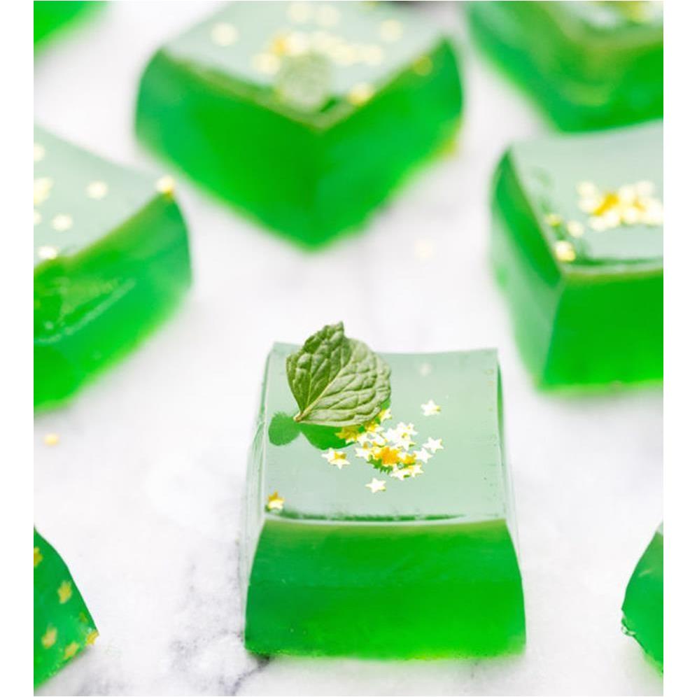 Des petits carrés de gelée verte avec au-dessus des paillettes en forme d'étoiles et une mini feuilles de menthe. Le tout sur table en marbre