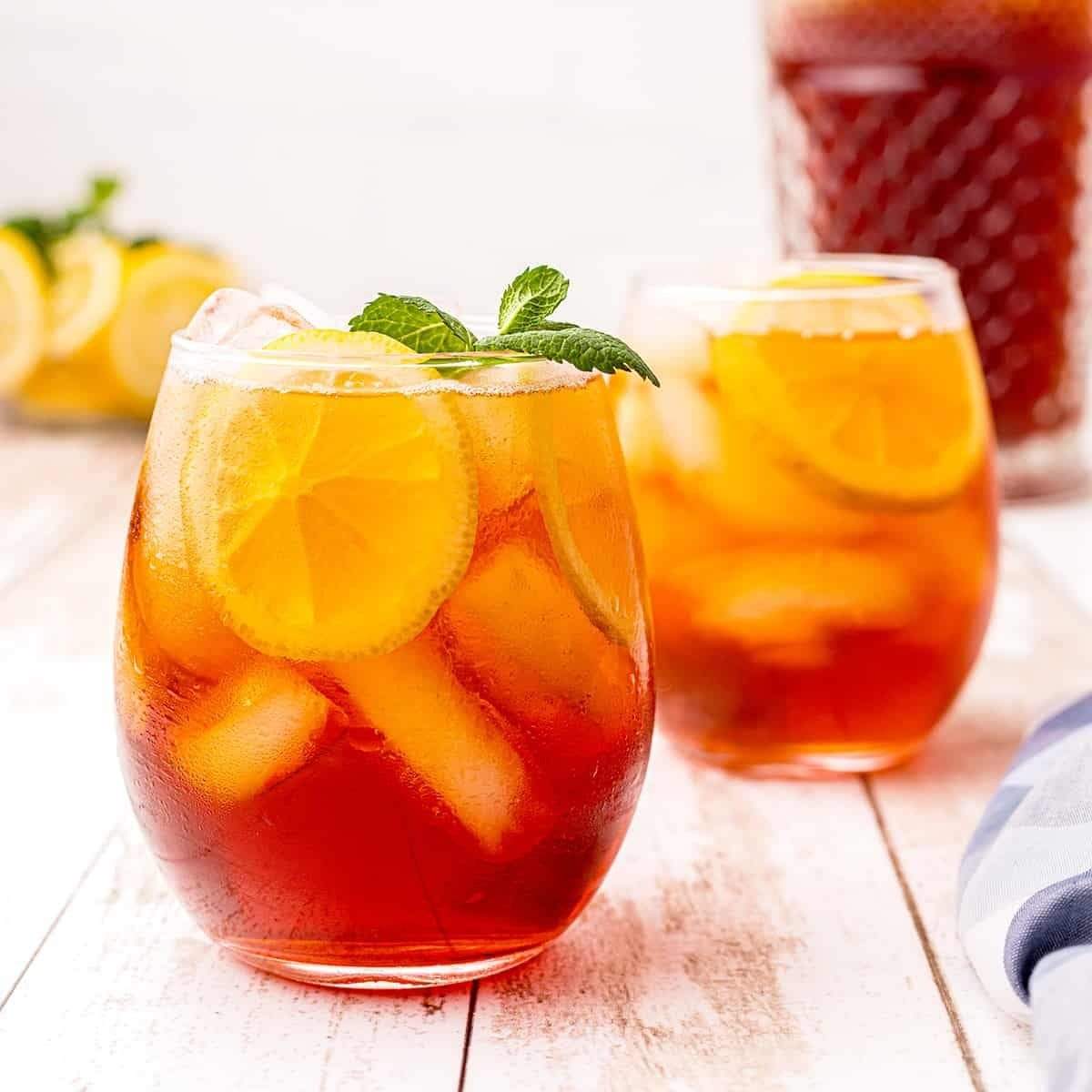 2 verres de thé glacé avec des glaçons et des morceaux de citrons jaunes. Le tout sur une table en bois