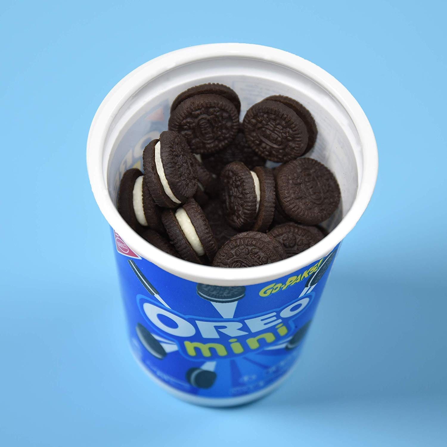 Un emballage blanc et bleu vu d’en haut, il est ouvert et il y a plein de biscuits noirs avec de la crème blanche à l’intérieur, le tout sur une table bleu