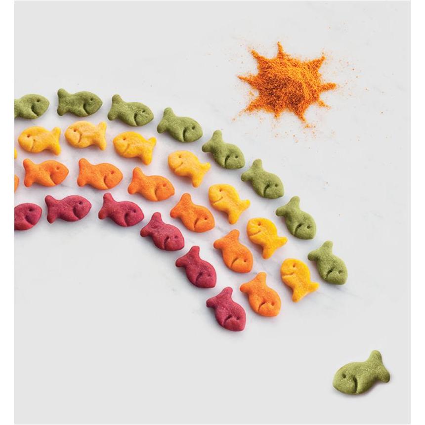 Des petits biscuits en forme de poisson disposés en arc-ciel, ils ont différentes couleurs ; vert, jaune, orange, rouge. Et haut il y a un soleil fait avec de la poudre orange, le tout sur fond blanc