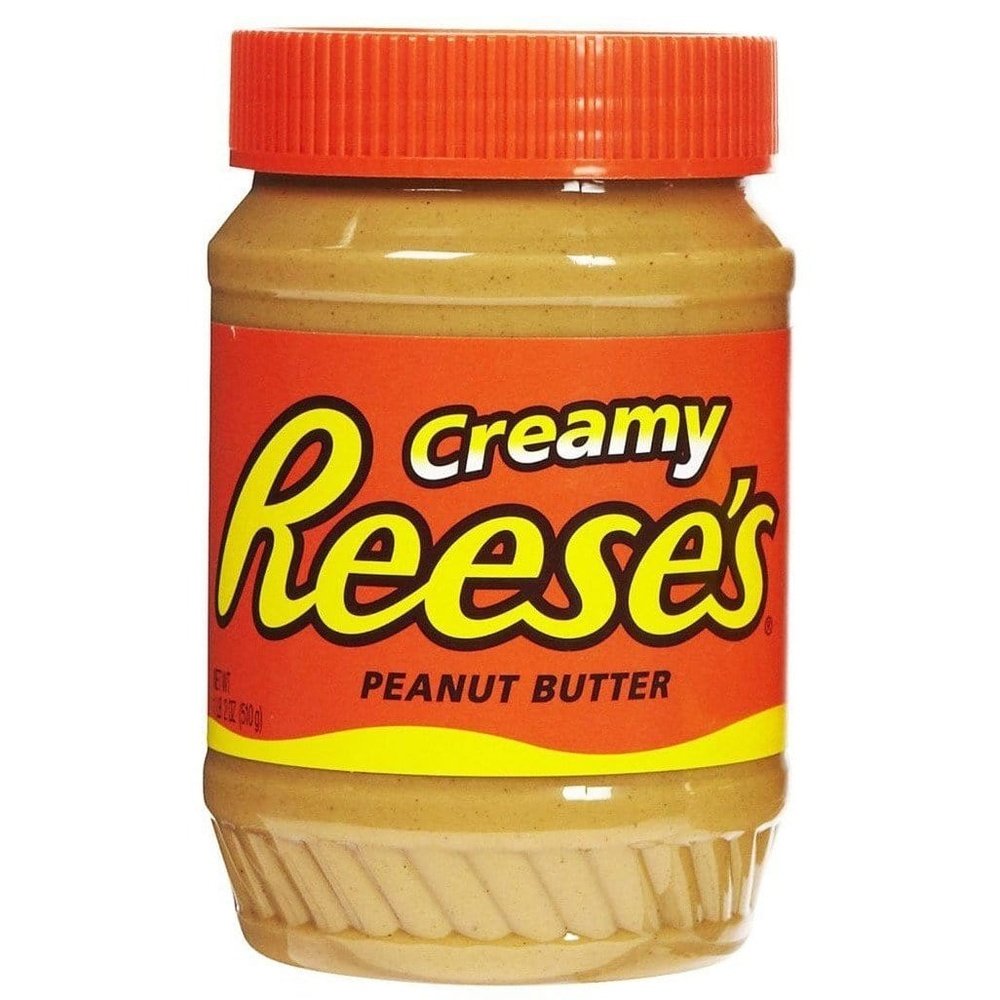 Un pot transparent avec une pâte brune claire, un capuchon orange et une étiquette orange avec écrit « Reese’s » en jaune. Le tout sur fond blanc